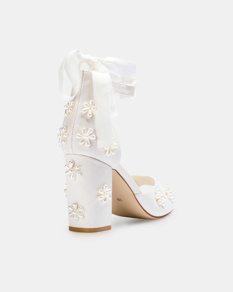 White high-heeled shoes with floral embellishments on a white background