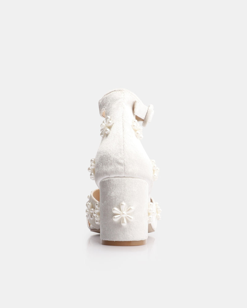 White high-heeled shoes with floral details on a white background