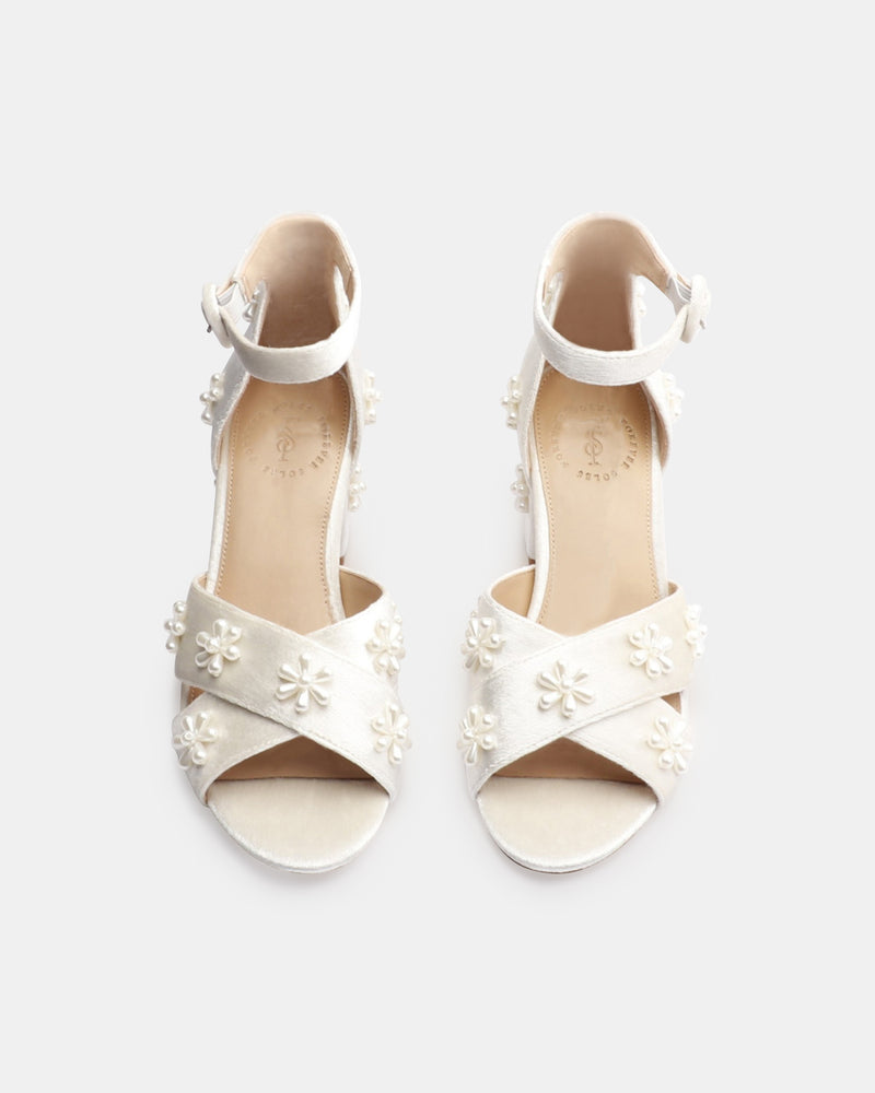 White high-heeled sandals with floral embellishments on a white background