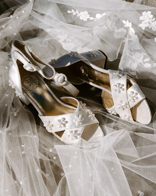 Pair of white high-heeled shoes with decorative flowers on a white fabric background