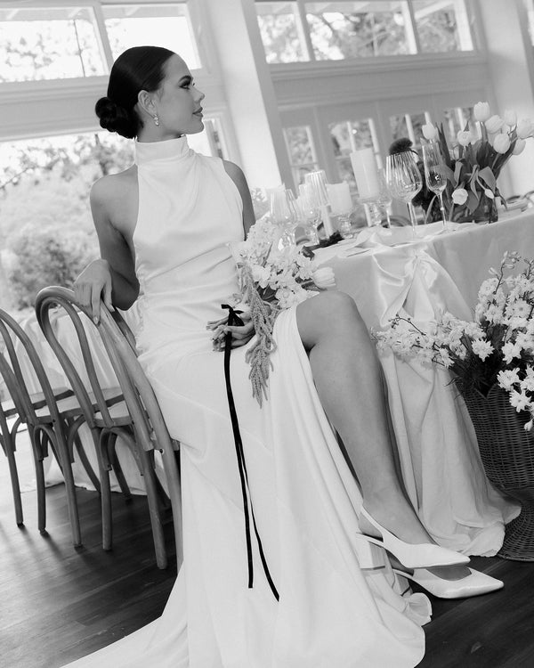 Woman in a bridal dress sitting on a chair with satin bridal shoes.
