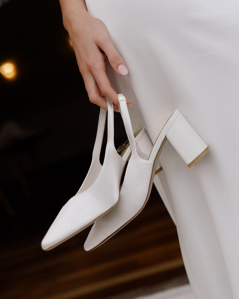White high-heeled shoes held by a hand against a blurred background