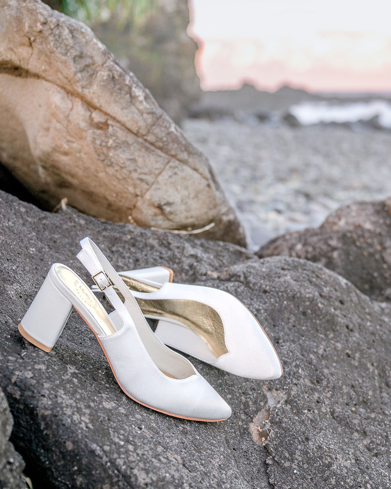 White high-heeled shoes with gold straps on a rocky surface