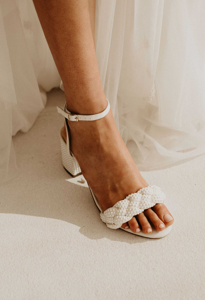 White sandal with pearl detailing worn by a person on a neutral background