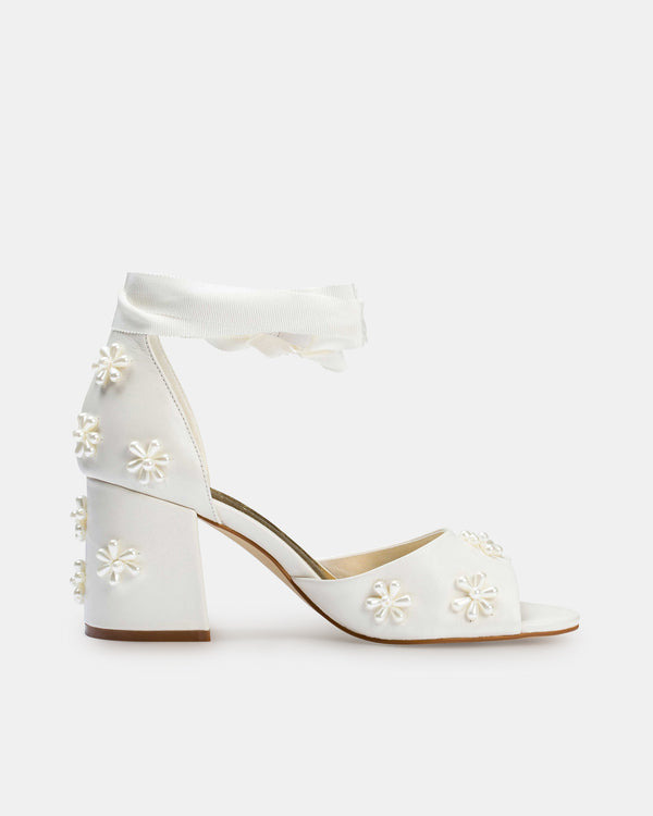 White high-heeled shoes with floral embellishments on a white background