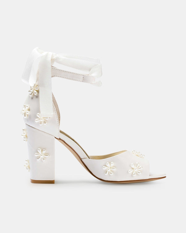 White high-heeled shoes with floral embellishments on a white background