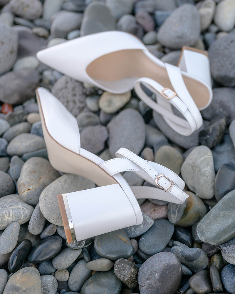White high-heeled shoes with beige soles on a pebbly surface