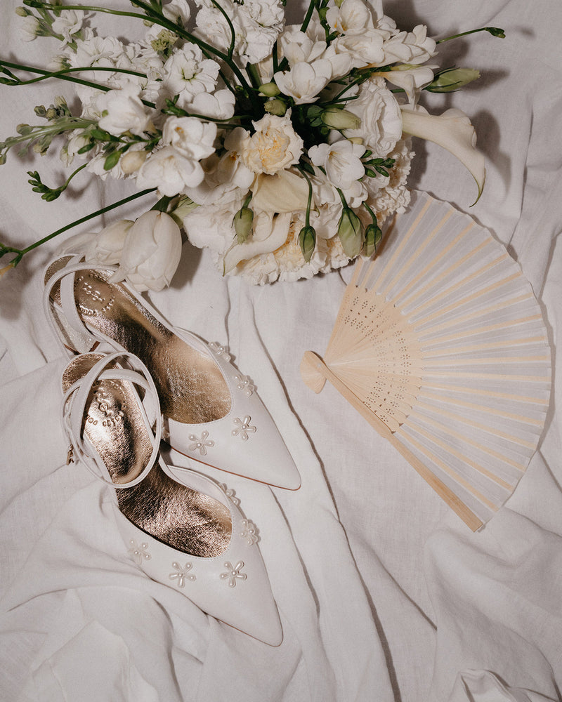 Bouquet of white flowers, gold shoes, and a beige fan on a light fabric background
