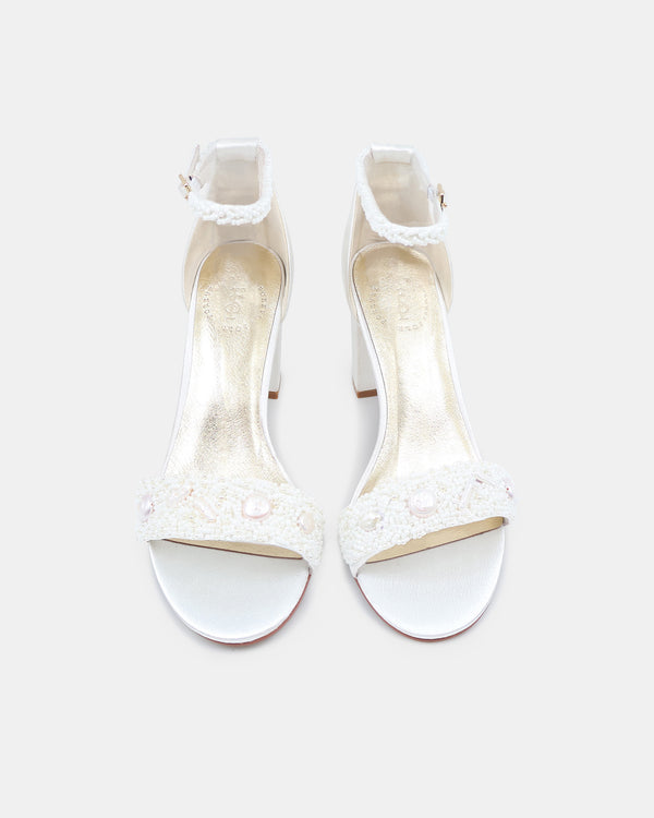 Pair of white high-heeled sandals with lace details on a light gray background