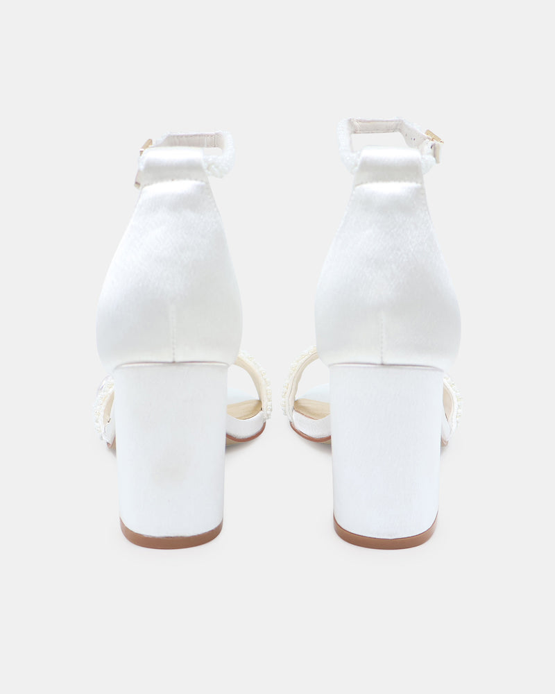White high-heeled shoes with ankle straps on a light gray background