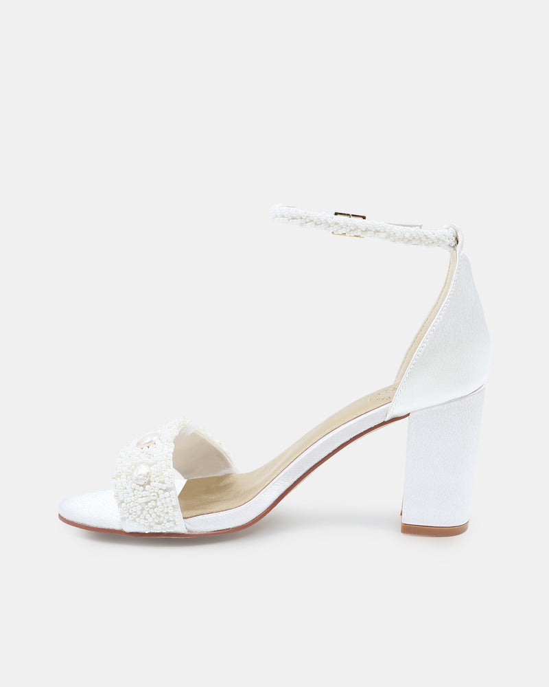 White high-heeled shoe with decorative elements on a light beige background