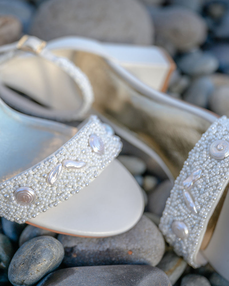 Ivory high-heeled shoes with bead embellishments on pebbles