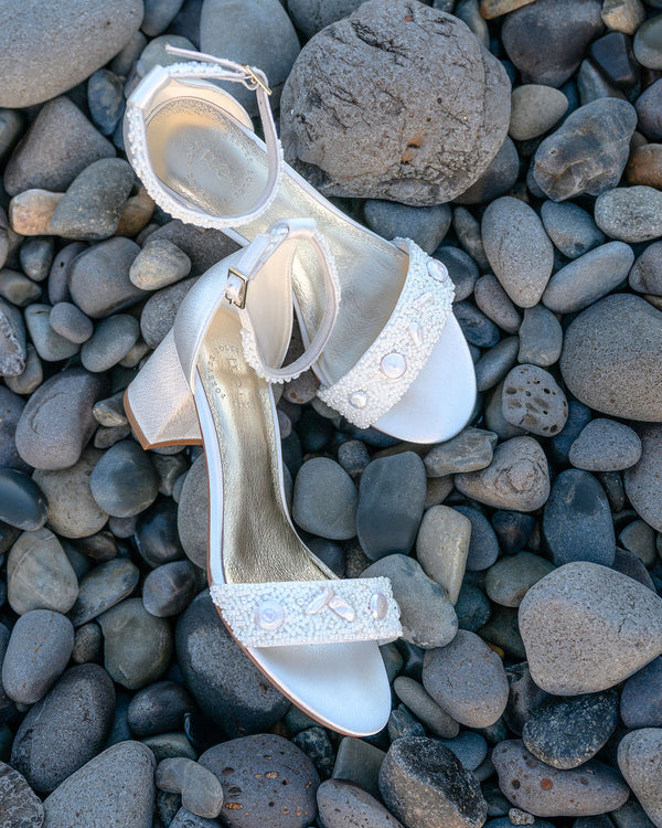 Pair of white high-heeled shoes with bead details on pebbles