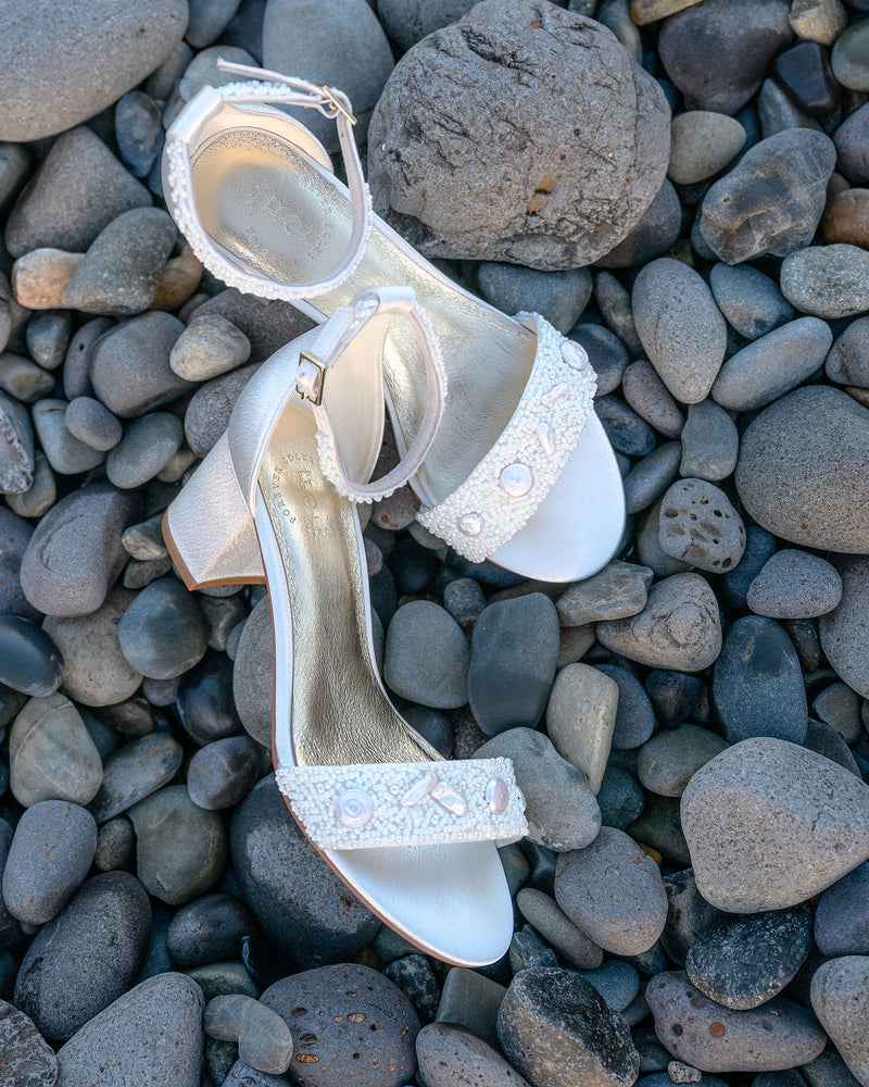 Pair of white high-heeled shoes with bead details on pebbles