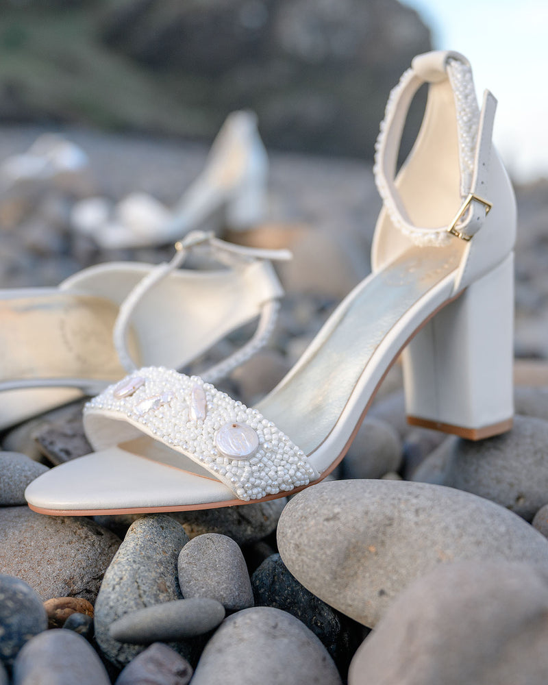 Ivory high-heeled shoes with bead embellishments on pebbles