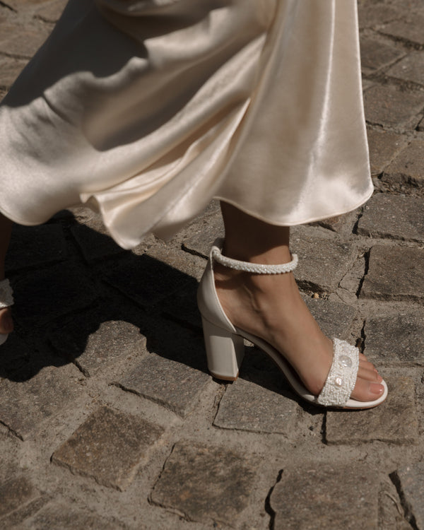 Ivory beaded sandals with pearl details worn on a stone pavement