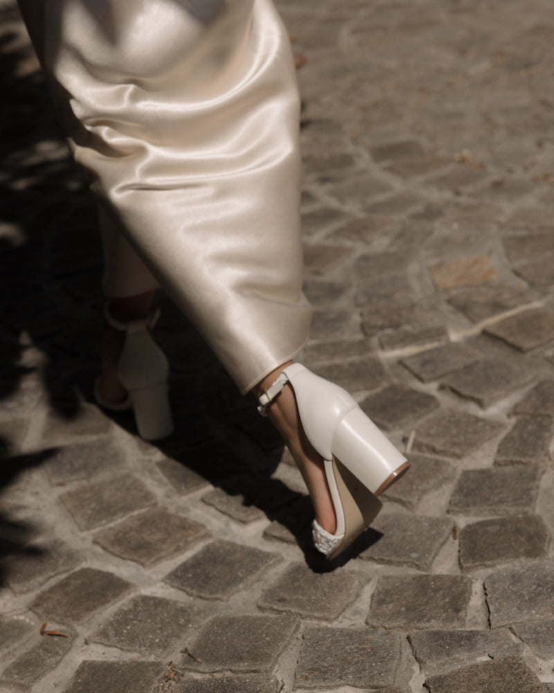 Ivory beaded sandals with pearl details worn on a stone pavement