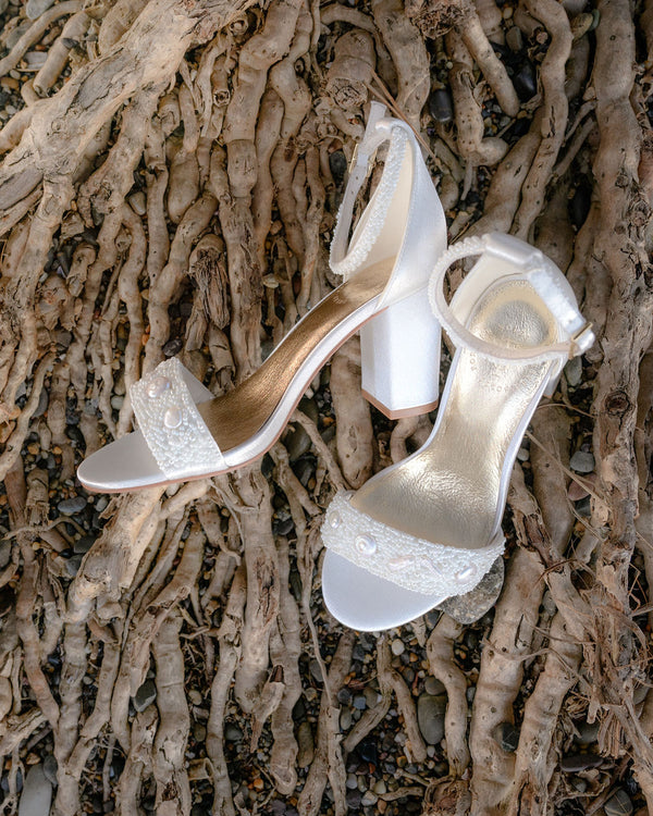 Pair of white high-heeled shoes with bead details on a textured surface