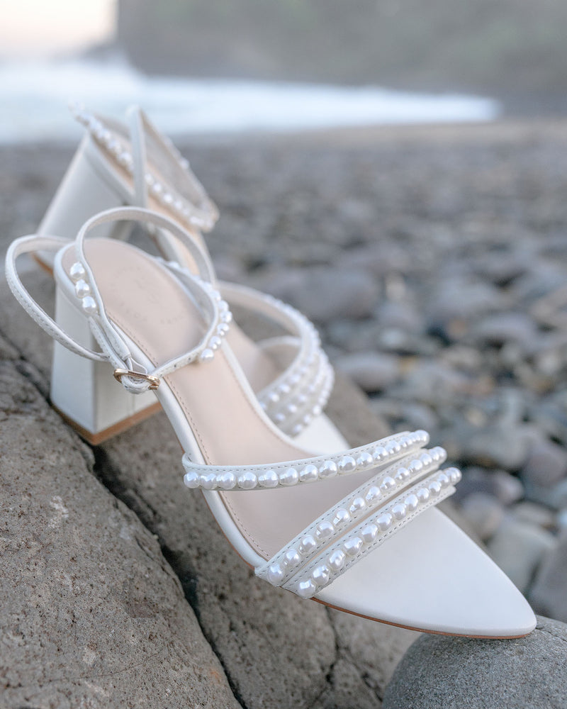 White high-heeled shoes with pearl detailing on a stone surface