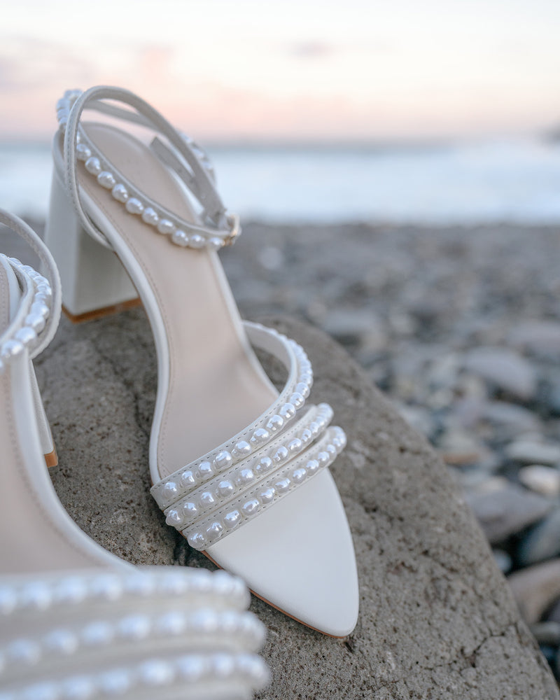 White wedding shoes with pearl embellishments on a pebble beach.