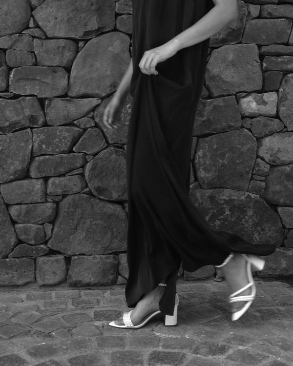 Person wearing a black dress and white sandals against a stone wall.